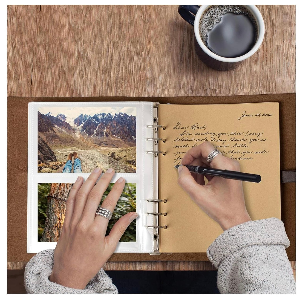 Person writing in a notebook with scenic photos and a cup of coffee on a wooden table.