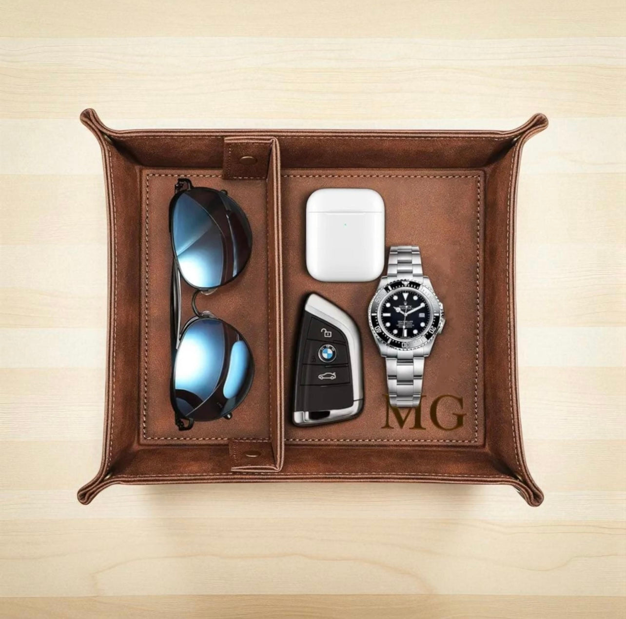 Brown leather tray with sunglasses, car keys, and watch on a beige background