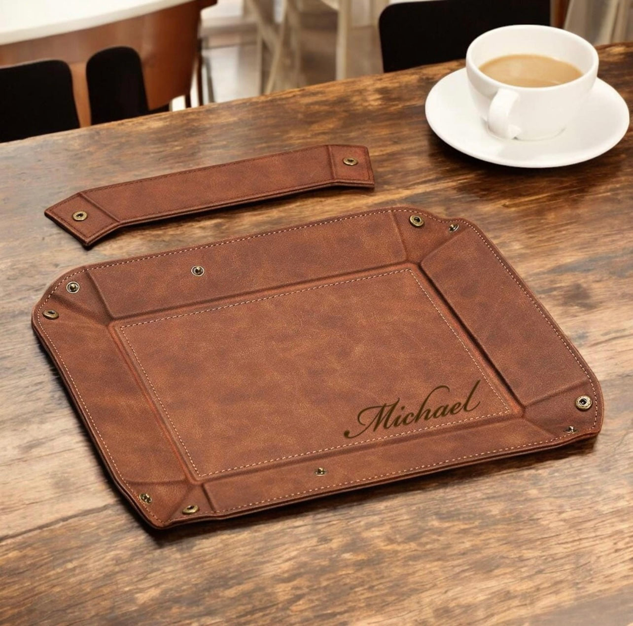 Brown leather tray with 'Michael' engraving on a wooden table with a cup of coffee.