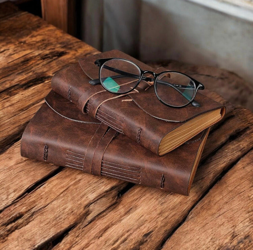 Two brown leather books with a pair of glasses on top, placed on a wooden surface.