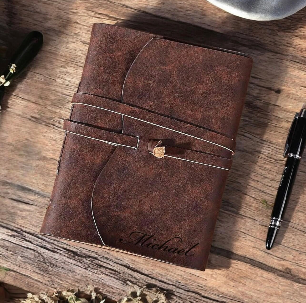 Brown leather notebook with 'Michael' engraving on a wooden surface with a pen.