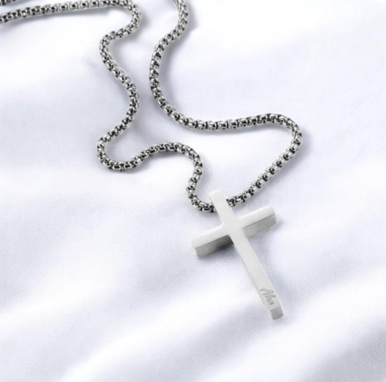 White cross pendant on a chain against a white background