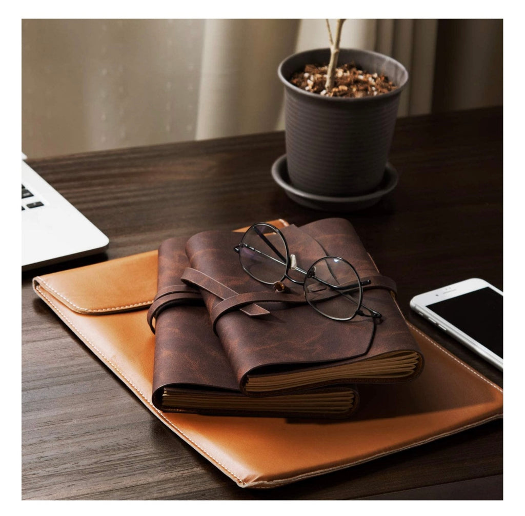 Brown leather notebook with glasses on a wooden desk with a plant and smartphone in the background