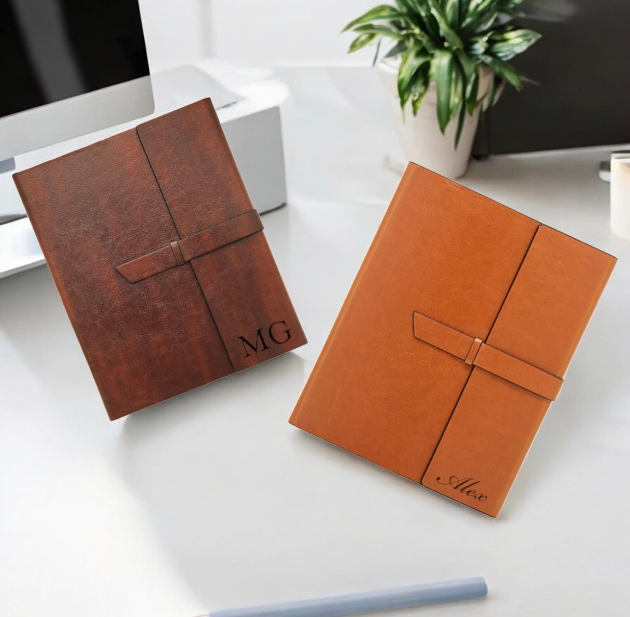 Two brown leather notebooks with monogram initials on a white surface.