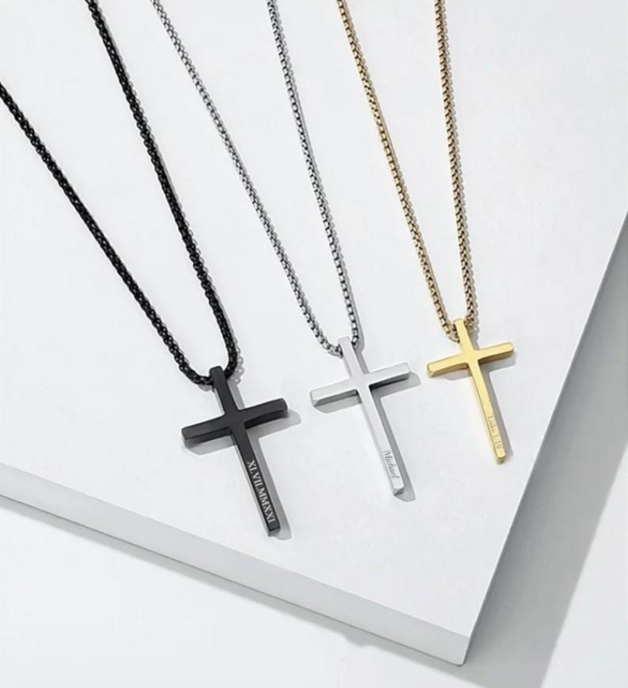 Three cross necklaces in black, silver, and gold on a white surface.
